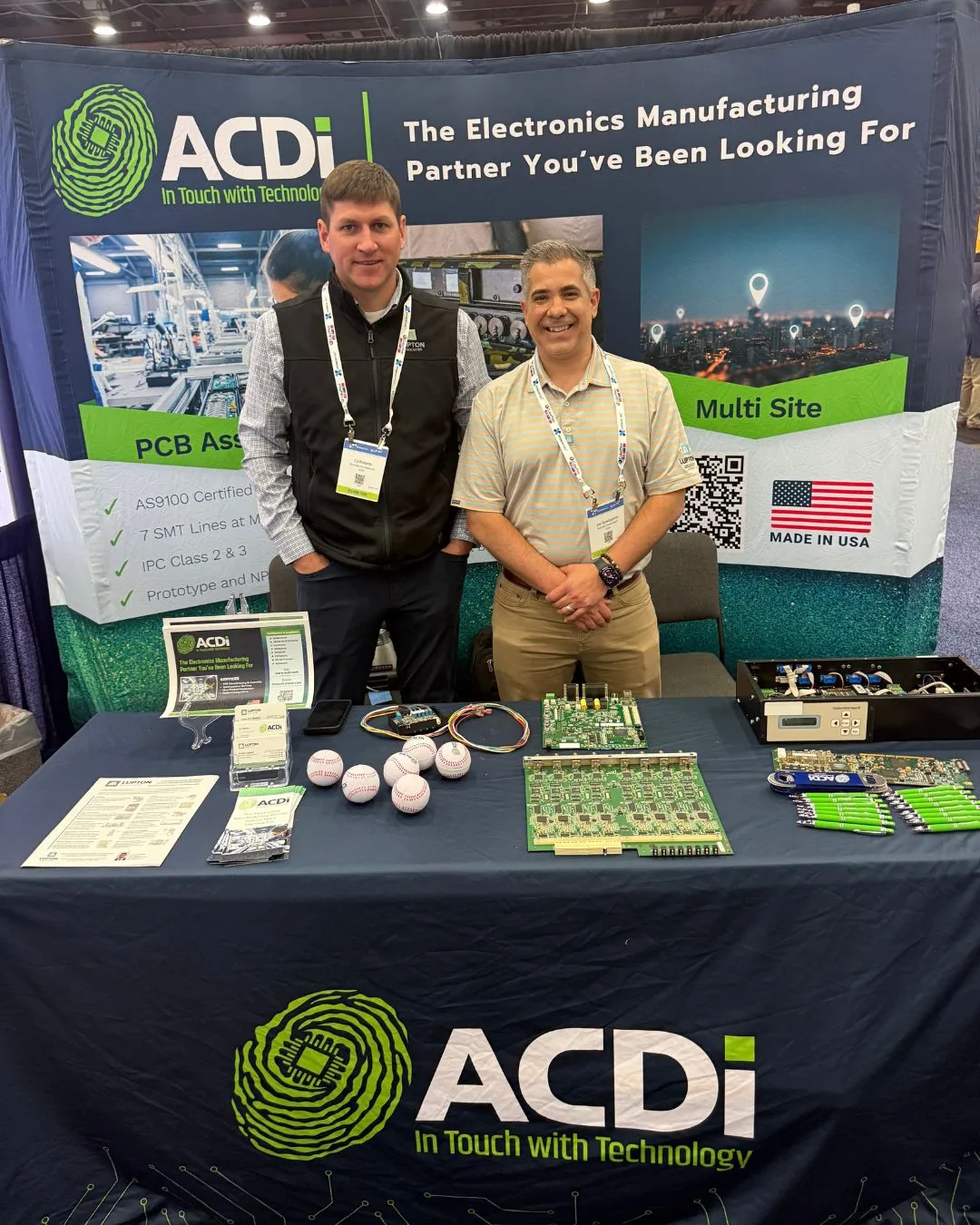 Two attendees standing at the ACDi electronics manufacturing exhibit during the XPONENTIAL event